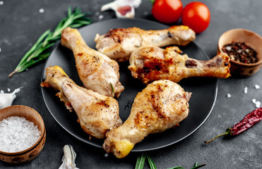 grilled chicken legs with spices on a black plate on a stone background