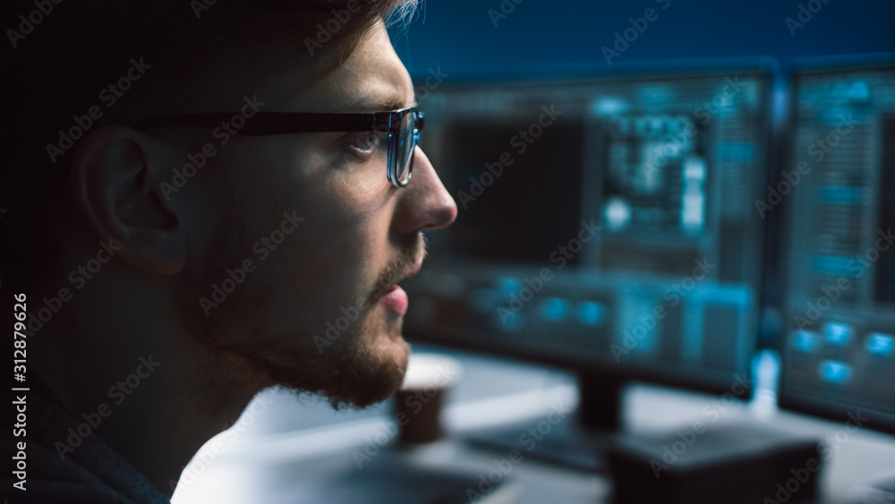 Poster Portrait of IT Specialist Wearing Glasses Works on Personal Computer with Screens Showing Software Program with Coding Language Interface. Dark Colors. Close-up Shot