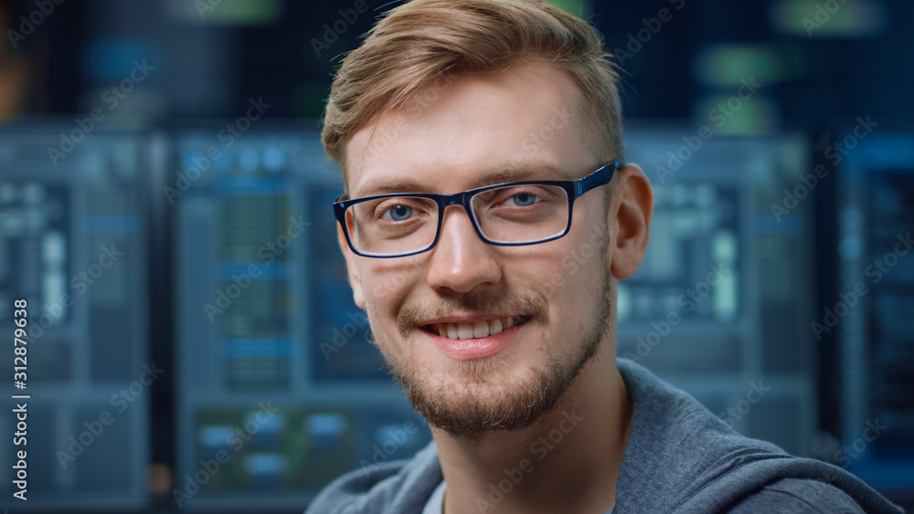 Poster Portrait of a Smart and Handsome IT Specialist Wearing Glasses Smiles at the Camera. In the Background Unfocused Personal Computers with Screens in Technological Research Data Center