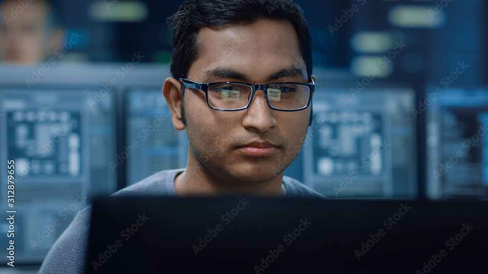 Poster Portrait of a Smart and Handsome IT Specialist Working on a Personal Computer. In the Background Bokeh Shot of Personal Computers with Screens in Technologically Advanced Data Research Center
