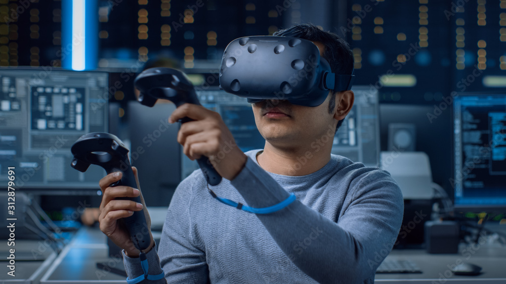 Poster Software Delevoper Wearing Virtual Reality Headset Using Controllers to Develop and Program VR Gaming and Applications. In the Background Technology Developing Studio with Computers and Monitors