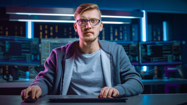 Portrait of Software Developer / Hacker Wearing Glasses Sitting at His Desk and Working on Computer in Digital Identity Cyber Security Data Center. Hacking or Programming.