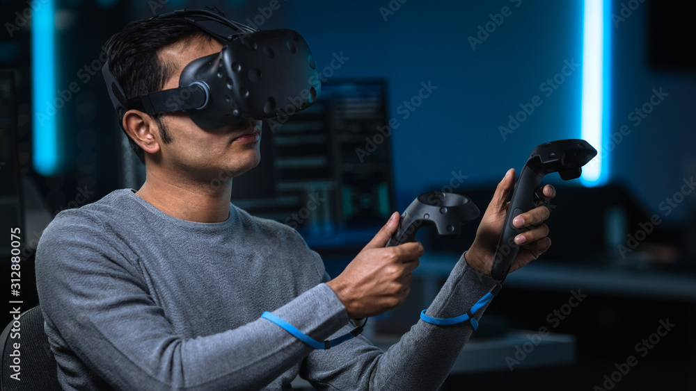 Aufkleber Portrait of Software Delevoper Wearing Virtual Reality Headset Using Controllers to Develop and Program VR Gaming and Applications. In Background Technology Developing Studio with Computer Monitors