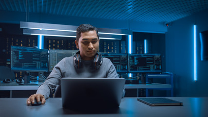 Portrait of Handsome Indian Software Developer / Hacker / Gamer Wearing Headset Sitting at His Desk...