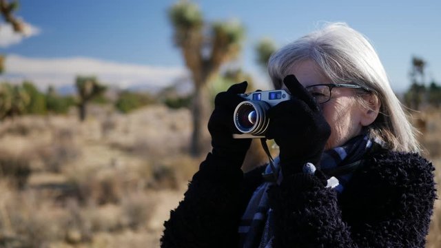 An adult woman photographer taking pictures with her old fashioned film camera in a desert wildlife landscape.
