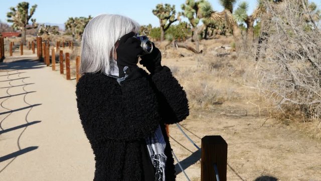 A woman taking photos with her old fashioned film camera and lens in a desert nature preserve park landscape.