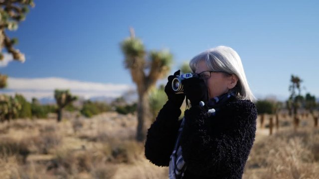 An older adult woman photographer taking pictures with her old fashioned film camera in a desert wildlife landscape.