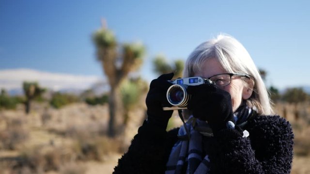 An adult woman photographer taking pictures with her old fashioned film camera and lens in a desert wildlife landscape CLOSE UP