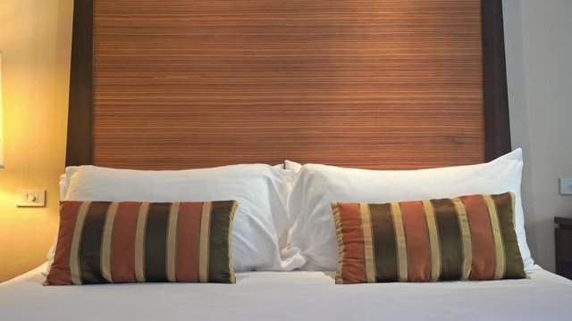 Tilt down shot of a hotel bedroom with a fresh and prepared bed, white sheets and pillows, two cusions in black and brown stripes.