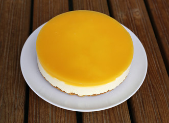 Gluten-free vegan orange and mango cheesecake created using vegan agar agar powder. Homemade cake with cookie base, mango cheese mousse layer and orange layer. Photographed on wooden balcony floor.