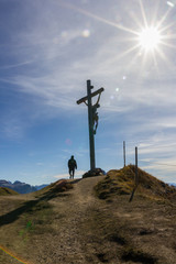 Silhouette of a Christian cross on the hill and a man walking towards it on a blue sky with sun halo