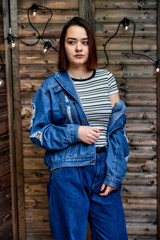 Portrait of a pretty brunette girl in denim suit on wooden background in alternative interior. Standing right in front of the camera in various poses.