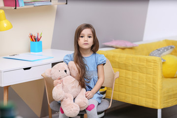 Cute little girl playing with toy bear at home