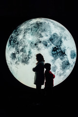 Silhouette picture of grandma and grandson stand on the mountain with A big full moon at night.