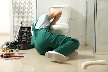Professional plumber repairing toilet bowl in bathroom