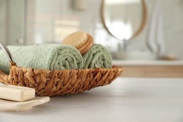 Wicker basket with rolled towels on white wooden table in bathroom. Space for text