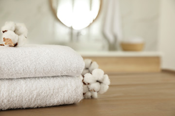 Stack of clean towels and cotton flowers on wooden table in bathroom. Space for text