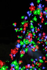 Close up of colorful light bulbs in a form of flowers on black background, Merry Christmas and Happy New Year concept. Amazing tree with shining garland of flowers.