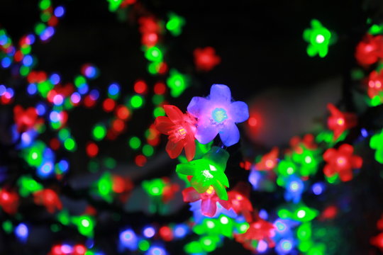Close up of colorful light bulbs in a form of flowers on black background, Merry Christmas and Happy New Year concept. Amazing tree with shining garland of flowers.