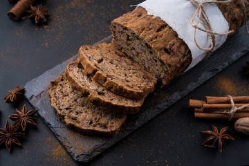 Sliced vegan homemade  banana bread with nuts and berry in the baking paper on the wooden table, selective focus.  cinnamon, anis stars around.