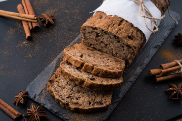 Sliced vegan homemade  banana bread with nuts and berry in the baking paper on the wooden table, selective focus.  cinnamon, anis stars around.