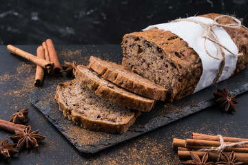 Sliced vegan homemade  banana bread with nuts and berry in the baking paper on the wooden table, selective focus.  cinnamon, anis stars around.