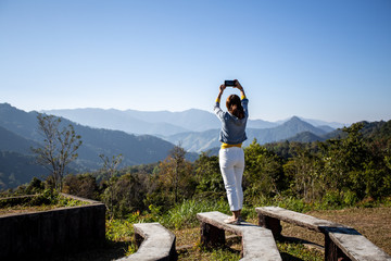 Fototapeta na wymiar Back view of a woman standing to take pictures of a beautiful mountain view with a smartphone ,Enjoy nature At the viewpoint of Chiang Mai, Thailand