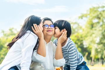 Happy Asian family relaxing in park. Cute young boy kid and mother kiss grandmother sitting on grass, closing eyes feeling happy and smile, spending happy time together. Recreation and rest on holiday