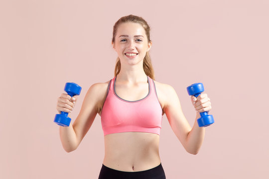 Beautiful young woman with dumbbells in her hands does fitness. Studio photoset on a pink background. © A Stock Studio