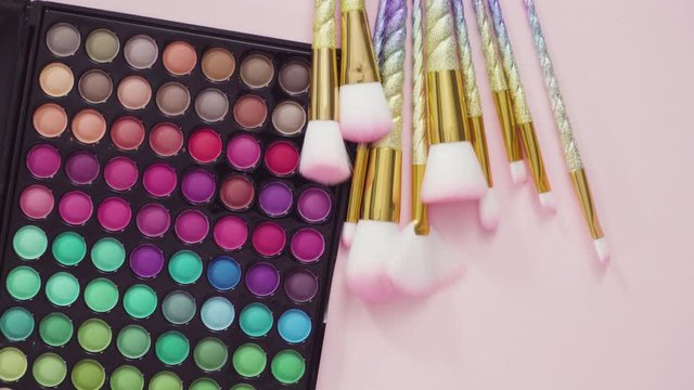 Flat lay. New eyeshadow palette with makeup brushes on a pink background.