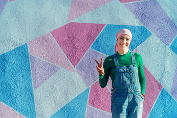 Woman with headscarf fights cancer on a colorful wall and showing victory shaped fingers