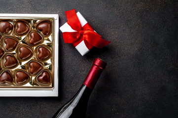 Heart shaped chocolates in a box, a bottle of wine and a gift with a red ribbon for Valentine's Day on a stone background with copy space for your text