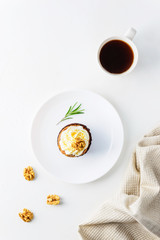 Cupcake with cream cheese, walnut, rosemary and a cup of coffee on a white table. Vertical orientation, top view.