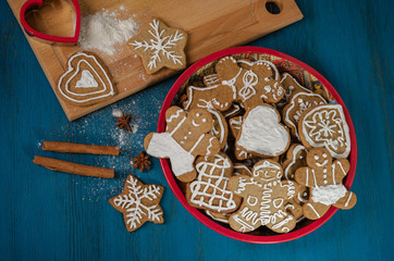 Gingerbread cookies of different shapes lying in a red dish on a blue wooden table.