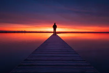 Fotobehang A man enjoying the colorful  dawn on a jetty in a lake. Groningen, Holland. © sanderstock