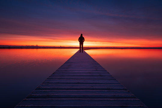 A man enjoying the colorful  dawn on a jetty in a lake. Groningen, Holland.