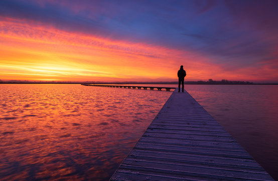 A man enjoying the colorful  dawn on a jetty in a lake. Groningen, Holland.