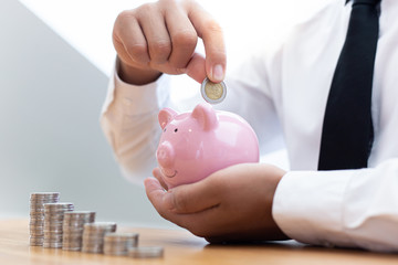 Hands holding coins placed in a piggy bank, Businessmen prepare a financial plan by accounting income - expenses for stable business growth saving ideas, Saving money concept