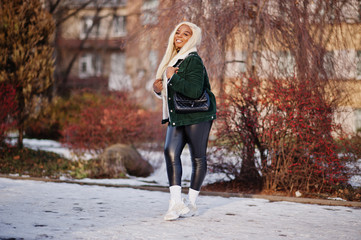 Chic african american blond woman in black leather clothes and green velvet jacket posed in winter sunny day.