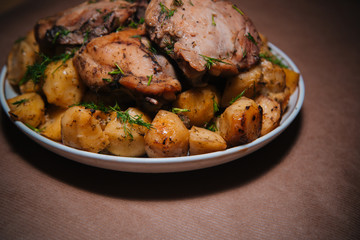Fried chicken legs with chips sprinkled with dill and greens on a large plate. Baked dish. Golden Potatoes