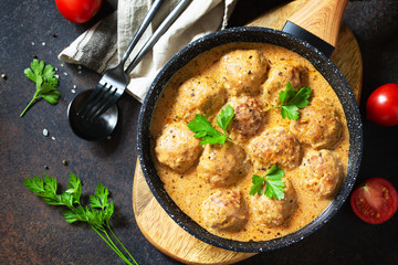 Meatballs in sour cream and tomato sauce in a pan on a dark stone or slate table. Top view flat lay background.