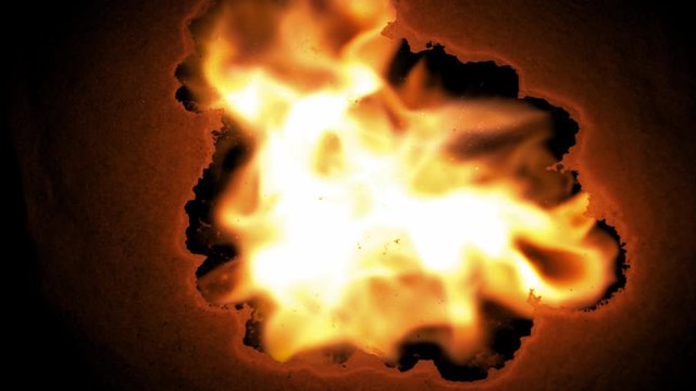 Close-up shot of burning paper of fire across the screen against a black background 