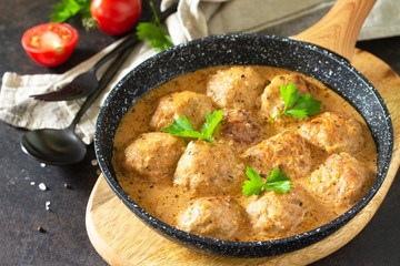 Meatballs in sour cream and tomato sauce in a pan on a dark stone or slate table.