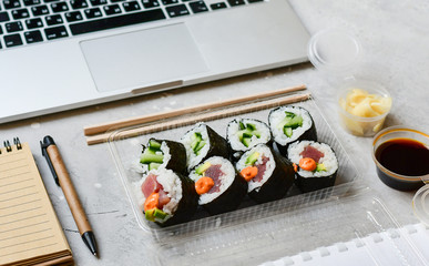 Food delivery. lunch box with sushi roll with tuna, avocado, cucumber and soy sauce on a gray office desk. takeaway lunch at the office. sushi menu delivery. Selective focus