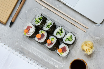 Food delivery. lunch box with sushi roll with tuna, avocado, cucumber and soy sauce on a gray office desk. takeaway lunch at the office. sushi menu delivery. Selective focus