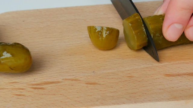 Female hands cut pickled canned cucumber on a rustic kitchen board with a black ceramic knife