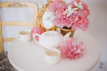 Tea table, mugs and a teapot white teapot with a pink bouquet of flowers in the rococo style....