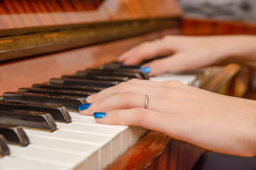Fototapeta premium hands of a female pianist with blue nail Polish on the nails on the keys of a piano. girl playing the piano.