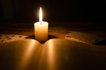 mystical atmosphere, cards, a book, a lighted candle in the dark on a wooden table. Esoteric...