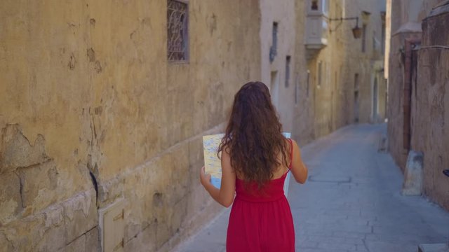 A young woman tourist is standing in the old city, with a map in his hands and looking for his whereabouts. Tourist with a map.